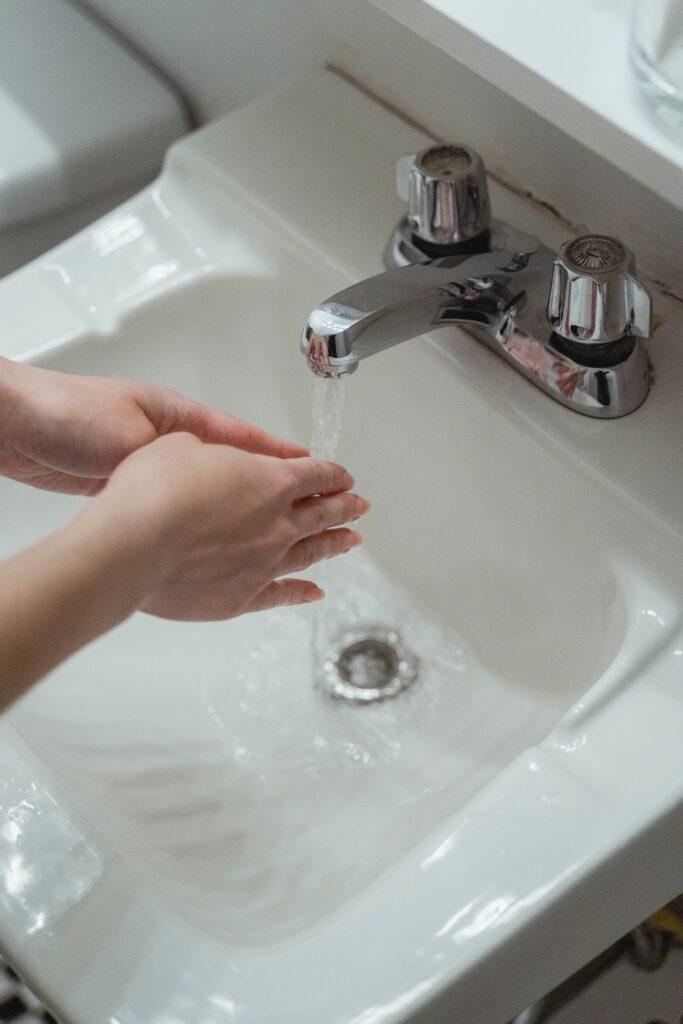 Person washing hands at sink with running water.