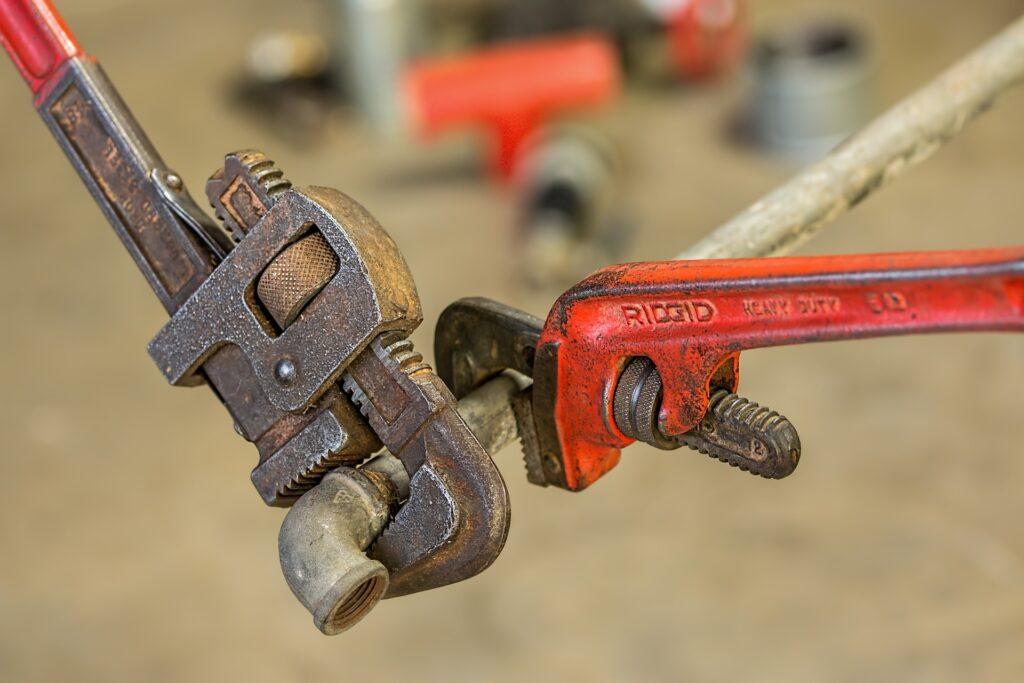 Two pipe wrenches gripping a metallic object.