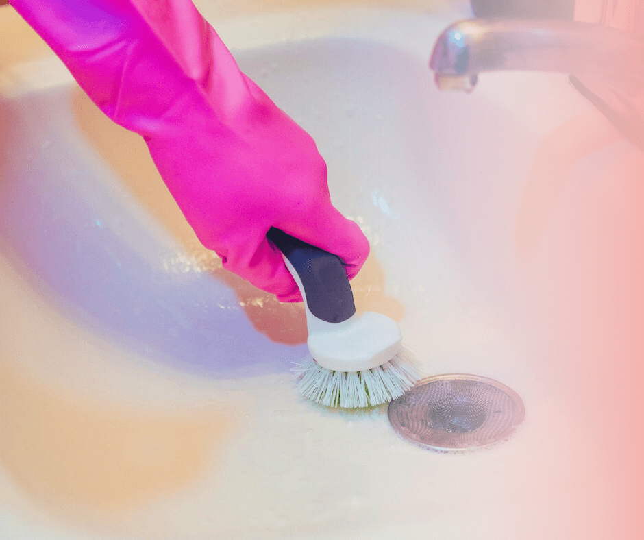 Scrubbing sink with brush wearing pink gloves