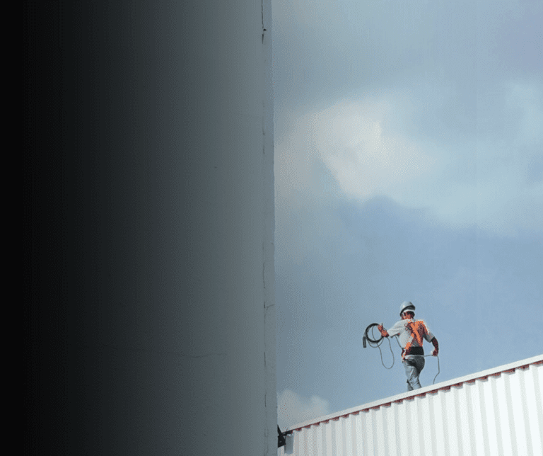 Worker on rooftop with safety harness against sky