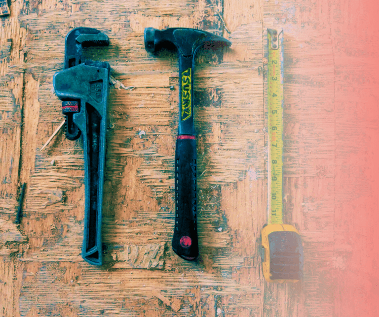 Pipe wrench, hammer, and tape measure on wooden surface.