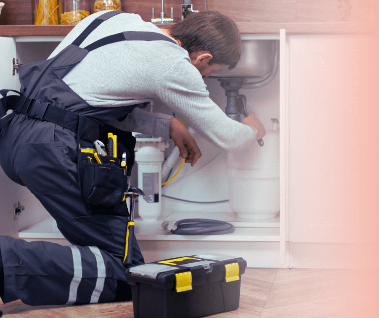 Plumber fixing sink pipes in kitchen.