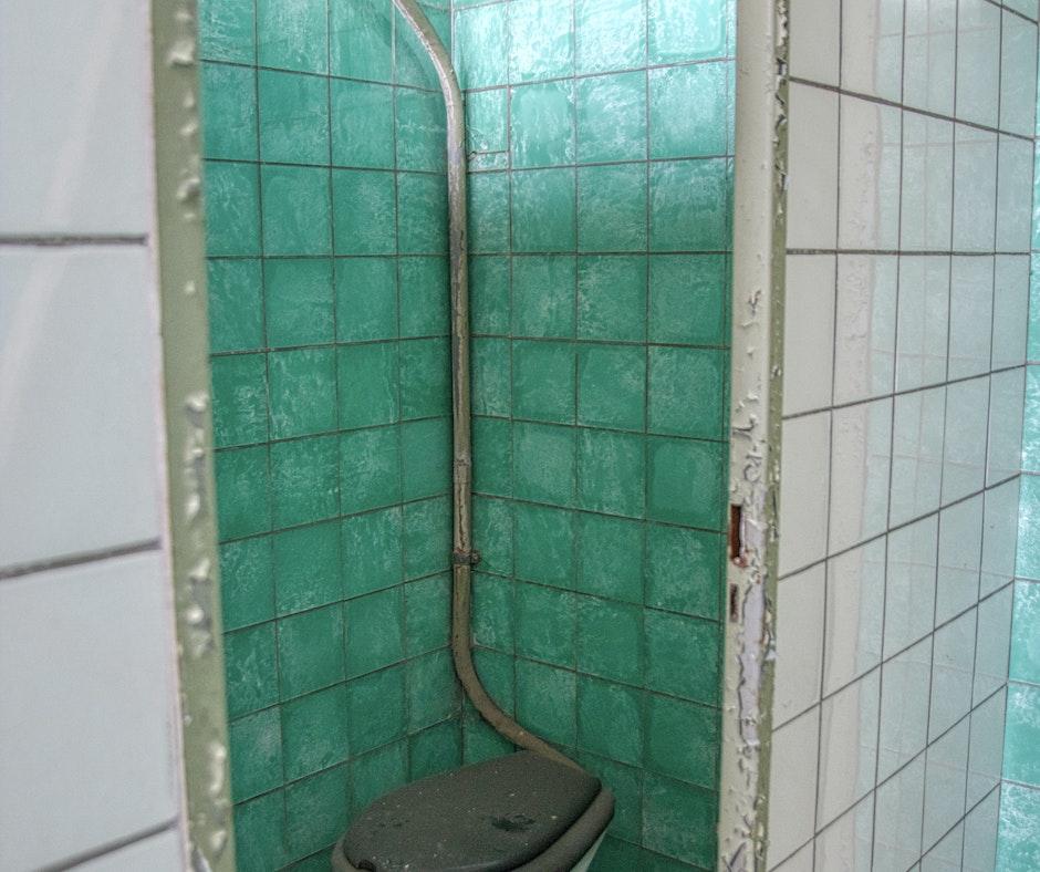 Old bathroom corner with teal tiles and toilet.