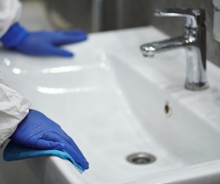 Person cleaning sink with blue gloves.