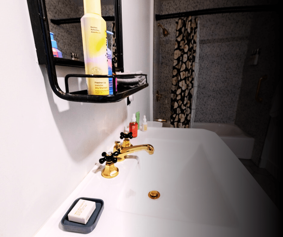 Bathroom interior with sink, faucet, and toiletries on shelf.