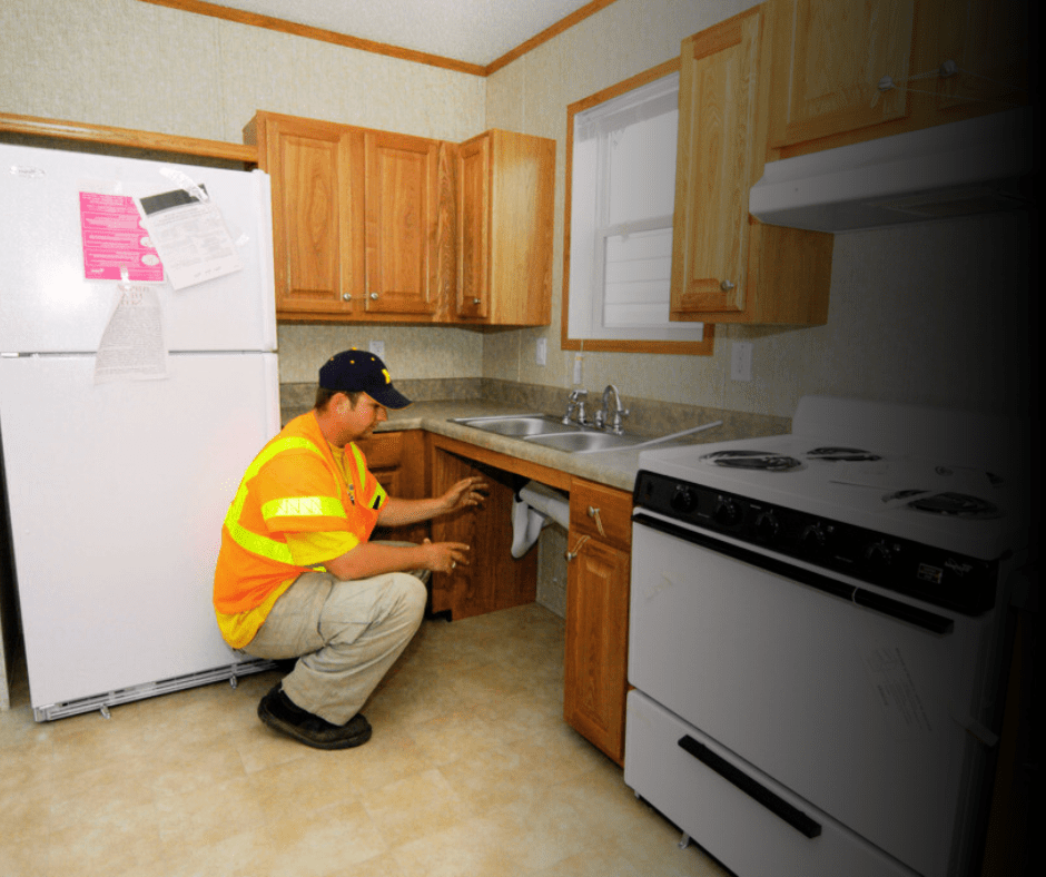 Worker inspecting kitchen plumbing under sink.