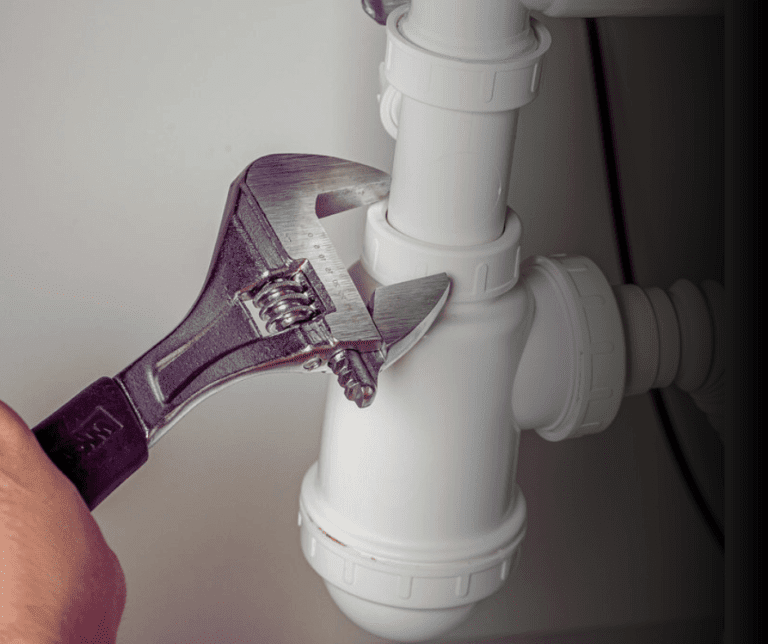 Adjustable wrench tightening white sink pipe.