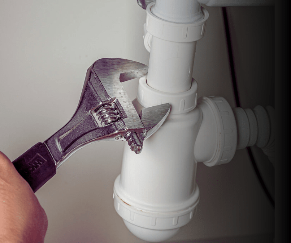 Adjustable wrench tightening white sink pipe.