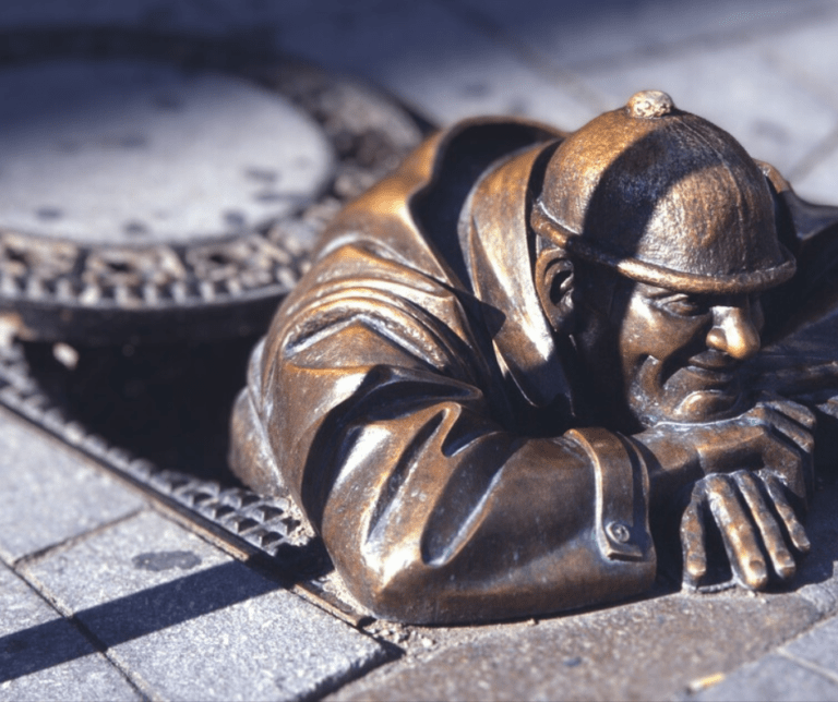 Bronze sculpture of a man emerging from sewer.